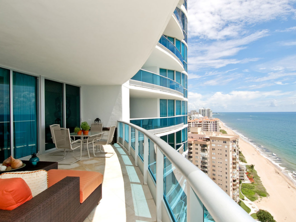 A balcony with chairs and tables overlooking the ocean.