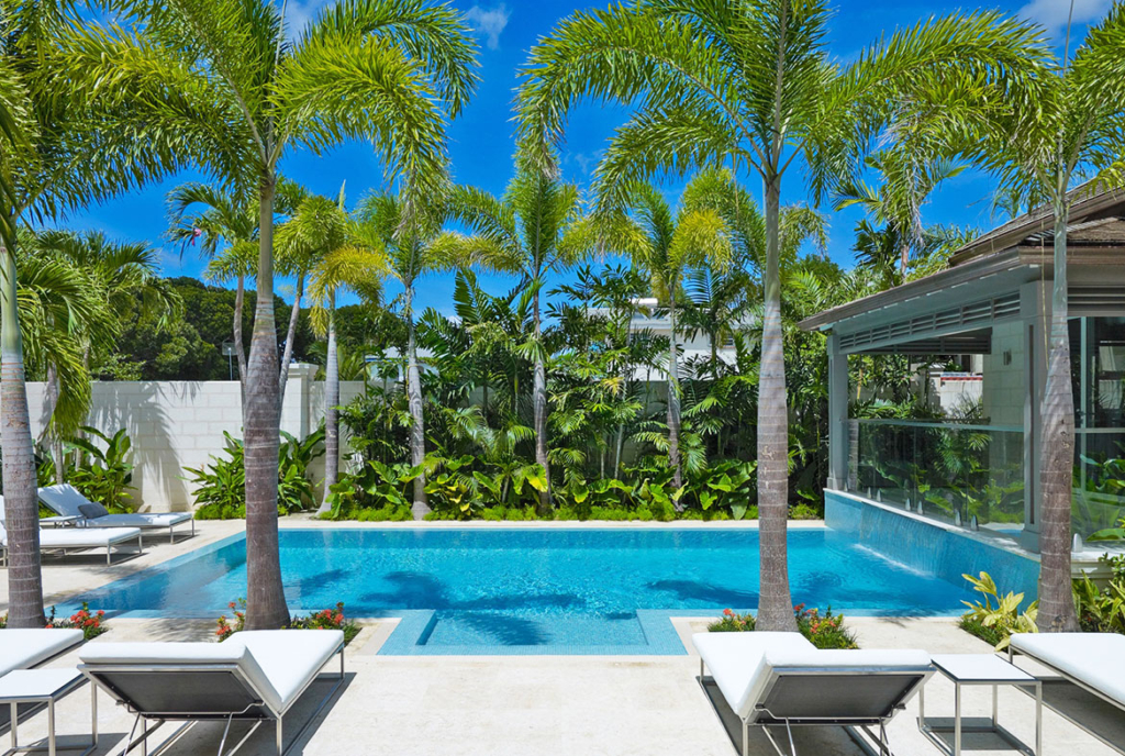 A pool with palm trees and chairs in the foreground.